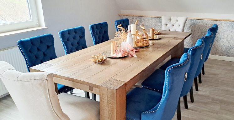 Holztisch mit blauen und weißen Stühlen, dekoriert mit Geschirr und Blumen.